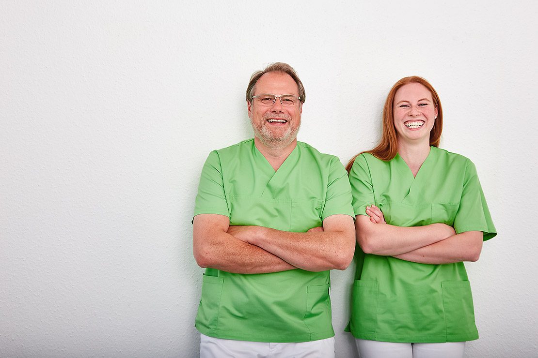 Christoph Schulte und Dr. Christina Schulte-Lohmann in grüner Praxiskleidung, lachend